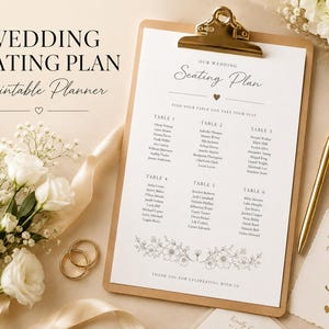 May include: A wedding seating plan printable template on a clipboard with a gold clip. The white paper features black text, a floral illustration at the bottom, and lists tables one through six with names. A gold pen and two gold rings are nearby.