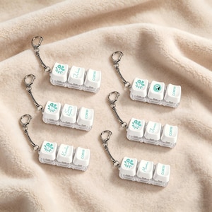 May include: Six keychains, each featuring three white mechanical keyboard keycaps attached to a metal ring. The first keycap displays a teal eye graphic, the second a name in cursive script, and the third the word CORTES in teal lettering.