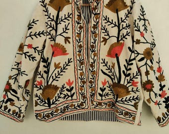 May include: An off-white jacket featuring a high collar and long sleeves, decorated with intricate floral embroidery in shades of brown, black, and coral. The garment has a front opening and a visible black and white striped inner lining.