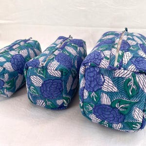 Peut inclure: Trois trousses rectangulaires à fermeture éclair de tailles différentes, présentant un motif en tissu matelassé avec des roses bleues, des feuilles vertes et des rayures blanches. Chaque trousse possède une fermeture éclair métallique argentée.