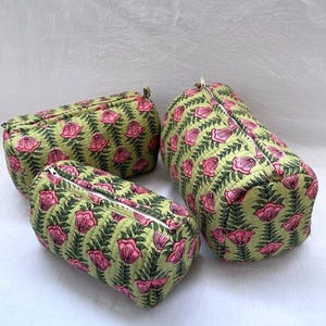 Puede incluir: Tres estuches de tela acolchada de diferentes tamaños, con un fondo verde claro y un patrón repetitivo de flores rosas y hojas verde oscuro. Cada estuche tiene una cremallera blanca en la parte superior y una textura suave y acolchada.