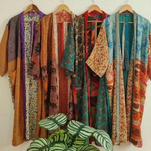 May include: Four long-sleeved open-front robes hanging side by side. Each robe features a unique patchwork design with various floral, geometric, and animal patterns in vibrant colours including orange, purple, teal, red, and yellow fabric panels.