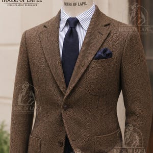 May include: A brown herringbone blazer featuring a two-button closure, notch lapels, and two patch pockets. The blazer is worn over a white and blue striped dress shirt with a solid navy blue necktie and a dark pocket square, displayed on a mannequin.