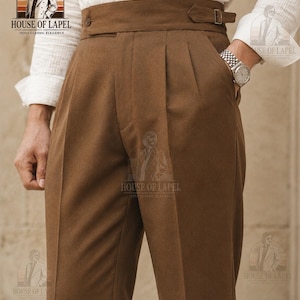 May include: High-waisted brown trousers featuring a wide waistband with a side buckle adjuster, double pleats at the front, and side pockets. The garment is paired with a white long-sleeved shirt. The text HOUSE OF LAPEL 1930s CLASSIC ELEGANCE is visible.