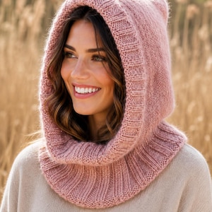 May include: A dusty rose knitted hood with a thick ribbed border that frames the face and extends down to cover the neck and shoulders. The headpiece features a soft, fuzzy texture and a consistent knit pattern throughout the entire garment.