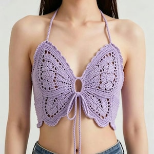 May include: A lavender crochet halter top featuring a butterfly-shaped design with intricate openwork patterns, a central circular cutout, and long adjustable tie strings at the front, paired with blue denim jeans.