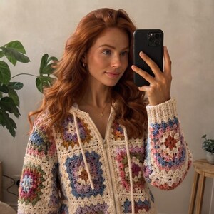 May include: A zip-up hoodie constructed from multi-coloured granny square crochet patches. The garment features a cream-coloured base with square motifs in shades of lavender, light blue, pink, and mustard yellow, complete with a hood and drawstrings.