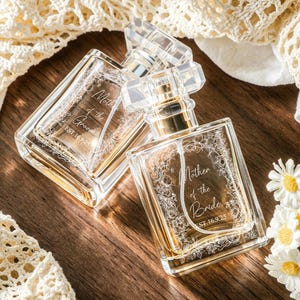 May include: Two clear glass perfume bottles with rectangular shapes and transparent caps. One bottle is engraved with Mother of the Groom EST.16.9.25 and the other with Mother of the Bride EST.16.9.25, both featuring intricate floral border designs.