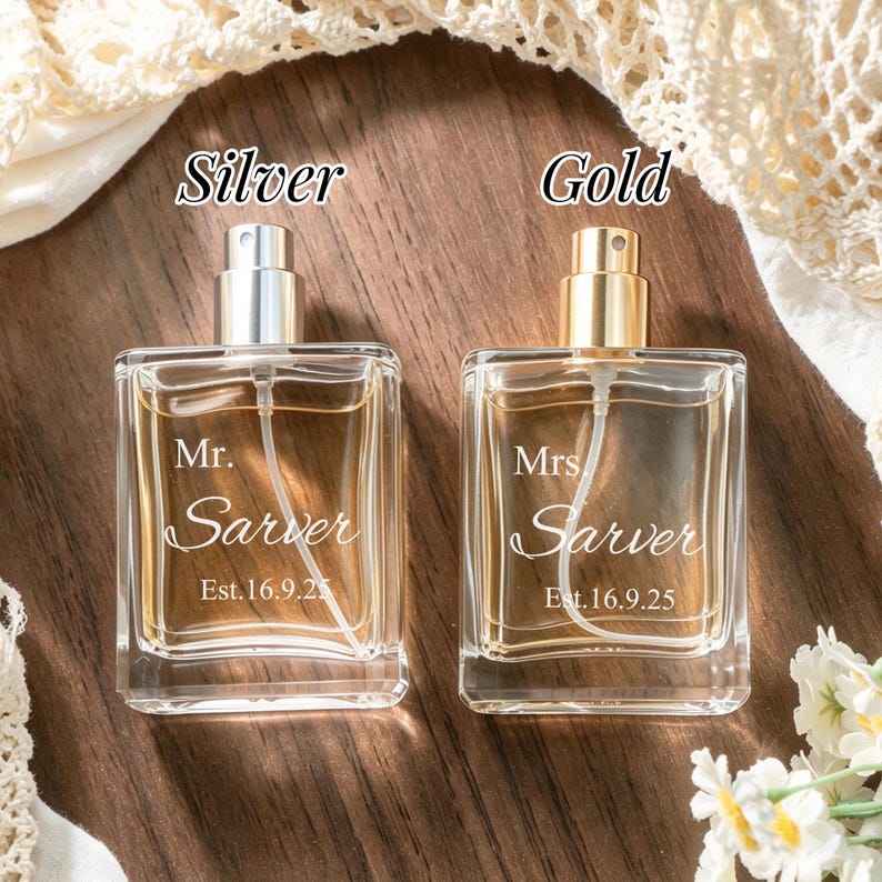 May include: Two square glass perfume bottles with spray nozzles. The left bottle has a silver cap and is engraved with "Mr. Sarver Est. 16.9.25". The right bottle has a gold cap and is engraved with "Mrs. Sarver Est. 16.9.25". Both contain amber liquid.