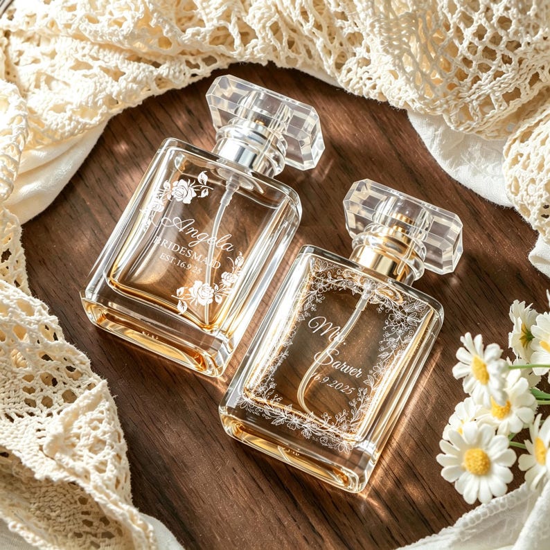 May include: Two rectangular glass perfume bottles with clear caps and gold-toned spray mechanisms. The left bottle is engraved with 'Angela BRIDESMAID EST. 16.9.2025' and floral accents. The right bottle features 'Mr. Sarver 16.9.2025' with a floral border.