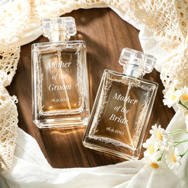 May include: Two rectangular glass perfume bottles with clear caps and spray nozzles. One bottle is engraved with "Mother of the Groom" and "16.9.2025", the other with "Mother of the Bride" and "16.9.2025". Both feature a delicate floral vine border.