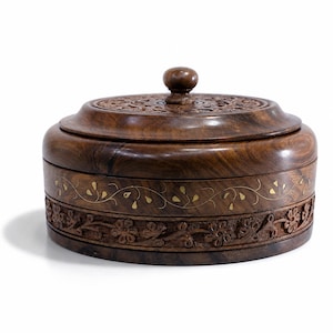 May include: A round dark brown wooden box with a matching lid featuring a central knob. The lid has intricate carved patterns. The side of the box displays a horizontal band of inlaid brass leaf motifs above a carved floral relief border.