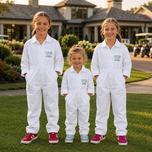 May include: Three white long-sleeved jumpsuits with collars, front pockets, and button closures. Each jumpsuit features black printed text on the chest that reads CUSTOM TEXT HERE, CUSTOM NUMBER. The jumpsuits have a straight-leg design.