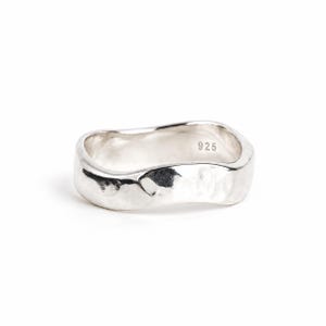 May include: A silver ring with an irregular, wavy band and a hammered, textured surface. The interior of the band is clearly stamped with the hallmark 925, indicating sterling silver composition. The metal has a polished, reflective finish.