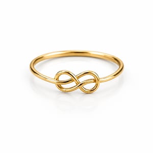 Könnte beinhalten: Ein polierter goldfarbener Ring mit einem Unendlichkeitssymbol in der Mitte. Die Ringschiene ist dünn und kreisförmig und geht vorne in die durchgehende, ineinander verschlungene Acht-Form über, was eine glatte, reflektierende Oberfläche ergibt.