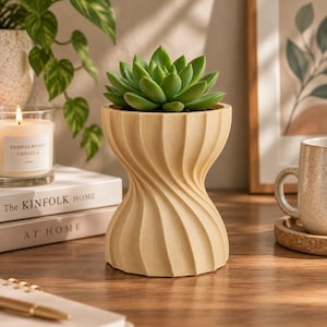 May include: A light beige planter with a vertical, spiraling, hourglass-shaped design. The planter features a smooth, matte finish and holds a vibrant green succulent plant with thick, pointed leaves arranged in a symmetrical rosette pattern.