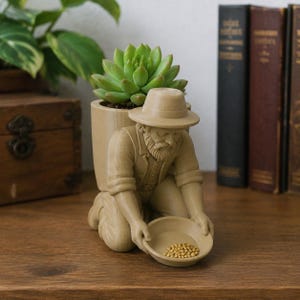 May include: A light brown planter shaped like a kneeling prospector wearing a hat and beard. The figure holds a small bowl containing gold-colored beads. A green succulent plant is potted in the cylindrical container attached to the prospector's back.