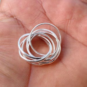 May include: A silver-colored ring composed of seven thin, interlocking circular bands. The metal has a smooth, polished finish, and the individual bands are connected to form a single, cohesive, multi-layered circular jewelry piece.