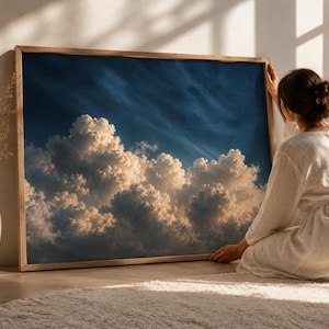 May include: A rectangular wall art piece featuring a high-resolution photograph of fluffy, sunlit cumulus clouds against a deep blue sky, encased in a simple light-toned wooden frame. The image captures the contrast between bright white cloud tops.
