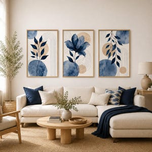 May include: A set of three framed wall art prints featuring abstract watercolor designs in shades of deep blue and beige. Each print displays botanical elements, including leafy branches and a large flower, layered over geometric circles and line art.