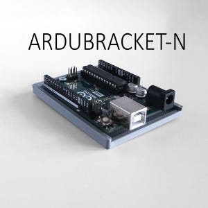 May include: An Arduino Uno R3 microcontroller board mounted in a grey 3D-printed plastic bracket. The board features black pin headers, a silver USB port, a black power jack, and integrated circuits. The text ARDUBRACKET-N is printed above the board.