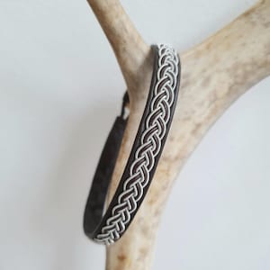 Puede incluir: Un brazalete de cuero marrón con un diseño trenzado plateado.