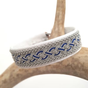 Könnte beinhalten: Weißes Lederarmband mit einem geflochtenen Design in Silber und Blau.
