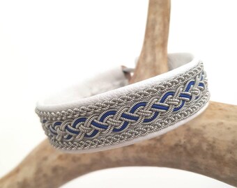 May include: White leather bracelet with a silver and blue braided design.