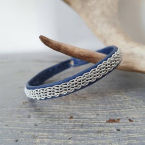 Può includere: Un braccialetto in pelle blu con un design intrecciato argentato.