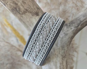 May include: A gray and silver braided leather bracelet with a woven design.