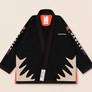 May include: A black martial arts gi jacket featuring orange interior lining, beige jagged side panels, and the text Oakley on the sleeves. The chest displays the text Albino & Preto, while a white label with the text A&P is attached to the front hem.