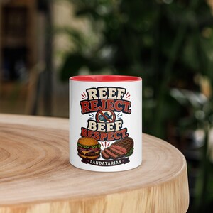 May include: A white ceramic mug with a red interior rim featuring a graphic illustration of a hamburger and sliced steak. The text reads REEF REJECT. BEEF RESPECT. LANDATARIAN, with a circular red prohibition symbol over a blue fish illustration.