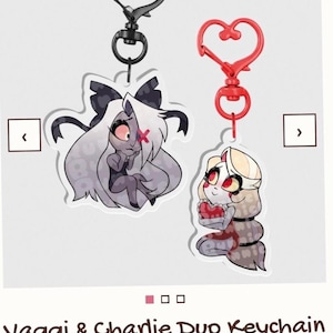 May include: A Vaggi & Charlie Duo Keychain Set featuring two acrylic charms with heart-shaped clasps. One charm shows a grey-haired character with a red eye patch, and the other shows a blonde character holding a red heart. Both have black outlines.