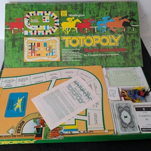 Könnte beinhalten: Ein Totopoly-Brettspielset mit einem grünen Schachteldeckel mit Pferderenn-Grafiken und dem Titeltext. Das Innere enthält ein gelbes Spielbrett mit Streckenfeldern, ein Regelheft, einen Stapel Flamenco-Karten und Spielfiguren aus Kunststoff.