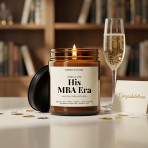 May include: A brown glass jar candle with a lit wick and a black lid. The label reads SMOKE & STORY, SMELLS LIKE His MBA Era, notes of case studies and big plans, 9oz SOY WAX CANDLE, VEGAN, HAND-POURED, DESIGNED IN NEW YORK, MADE IN USA. A champagne flute stands nearby.