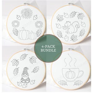 Op de afbeelding: Een 4-pack borduurringen met witte stof en zwarte lijntekeningen. De ontwerpen bevatten een krans van pompoenen en zonnebloemen, een eekhoorn met eikels en bladeren, een kabouter met bladeren en een pompoen in een mok met opstijgende stoom.
