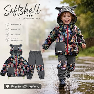 May include: A softshell adventure set consisting of a hooded jacket and pants. The jacket features a black base with a colorful cartoon character print, a red zipper, and animal ears on the hood. The solid gray pants have matching print patches.