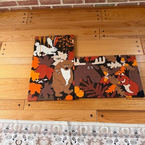 May include: Two rectangular canvas wall art pieces featuring forest animals. The vertical piece shows a white rabbit and a brown bear among orange and brown autumn leaves. The horizontal piece depicts a moose and a squirrel with acorns.