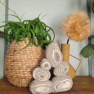 May include: A decorative sculpture composed of five stacked, smooth, rounded stones featuring concentric gray and white circular patterns. The stones are arranged in a pyramid-like formation with two base stones, two middle stones, and one top stone.
