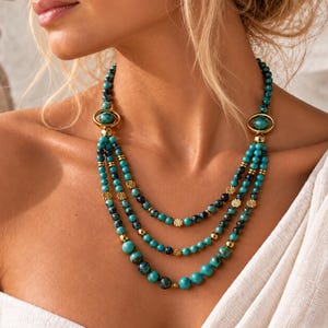 May include: A multi-strand necklace featuring turquoise and dark blue marbled beads interspersed with small gold-toned spacers and circular gold-toned accents. The design includes three cascading layers of beads connected by two oval gold-toned rings.