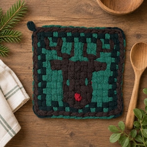 May include: A square woven potholder featuring a dark brown reindeer silhouette centered against a green and dark green checkered background. The reindeer design includes a small, bright red nose detail, and the potholder has a small loop.