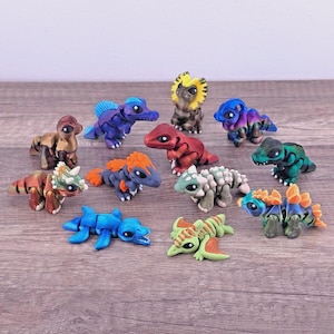 May include: A collection of eleven small, articulated dinosaur figurines in various colors including blue, green, red, brown, and orange. Each creature features a segmented body design, large dark eyes, and distinct prehistoric shapes.