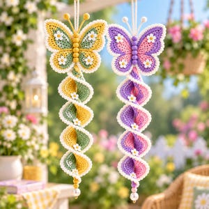 May include: Two hanging crochet butterfly wind spinners. One features yellow and sage green yarn with white daisy accents, while the other displays purple and pink yarn with white daisy accents. Both have beaded antennae and a pearl bead at the base.