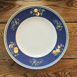 May include: A blue and yellow ceramic dinner plate with a lemon motif. The plate has a white centre and a blue rim with a yellow and white border.