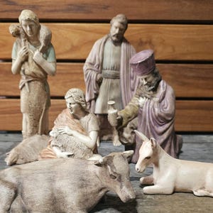 May include: A religious nativity scene featuring several figures and animals. The figures include a shepherd with a sheep, a man in a robe, a woman holding a sheep, and a kneeling man. Animals include a cow and a donkey.