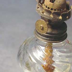 May include: A vintage glass oil lamp with a clear glass reservoir and a brass wick holder. The lamp has a decorative swirl pattern on the glass and a brass cap with a metal knob.