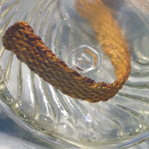 May include: A close-up of a clear glass bottle with a textured surface. A brown, woven fabric strip is inside the bottle.