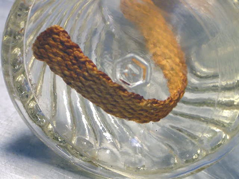 May include: A close-up of a clear glass bottle with a textured surface. A brown, woven fabric strip is inside the bottle.