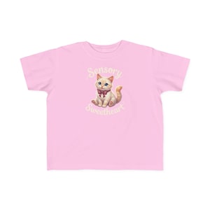 Peut inclure: Un t-shirt rose clair à manches courtes avec un motif central représentant un chaton crème portant un nœud papillon rouge foncé. Le chaton est entouré du texte Sensory Sweetheart écrit dans une police cursive décorative et incurvée.