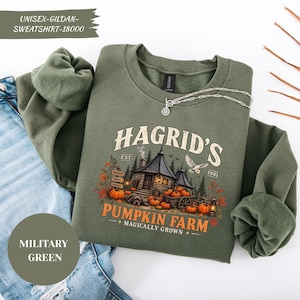 May include: A military green crewneck sweatshirt featuring a graphic print of a stone hut, pumpkins, a white owl, and the text "Hagrid's Pumpkin Farm Magically Grown Est. 1981". The sweatshirt has long sleeves with ribbed cuffs and a soft fleece interior.